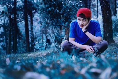 Full length of young man sitting on tree trunk