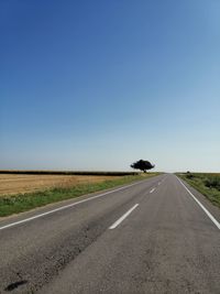 Road amidst field against clear blue sky