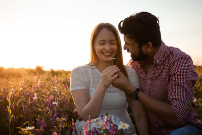 Young couple smiling on field against sky