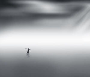 Silhouette man walking in river water under mist at dawn