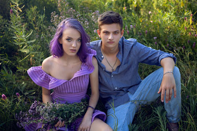 Lovers are a beautiful guy with a girl with purple hair and bouquet of flowers sitting on the grass