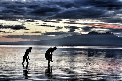 Silhouette people on sea against sky during sunset