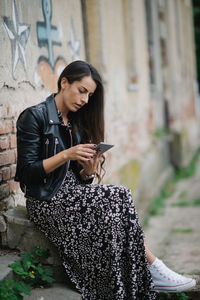 Bussineswoman with leather jacket and dress looking at her phone.