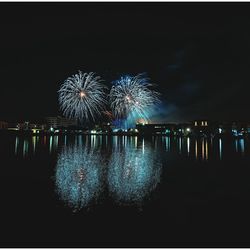 Illuminated firework display over lake against sky at night