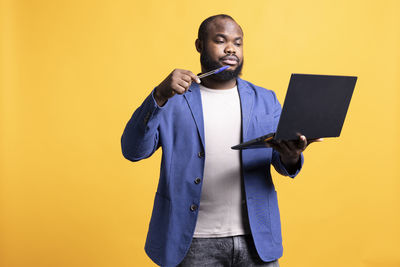 Portrait of young man using mobile phone against yellow background