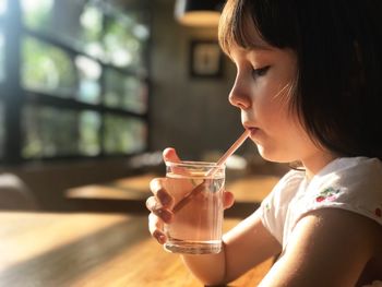 Profile view of girl drinking water while sitting at table