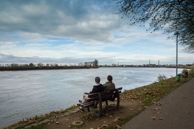 Man sitting on riverbank against sky