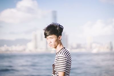 Young man standing by river against sky