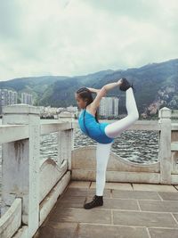 Full length of ballet dancer stretching leg while standing on building terrace