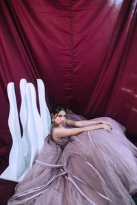 High angle portrait of woman wearing dress sitting against curtain