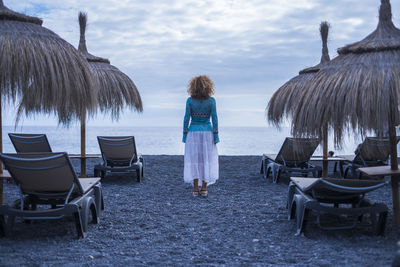 Rear view of man standing at beach against sky