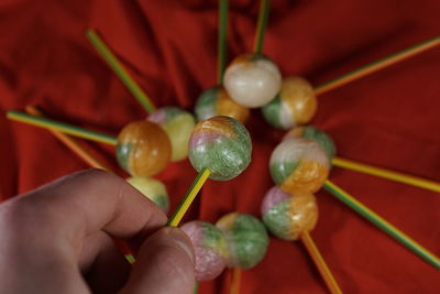 Cropped hand holding colorful lollipop over red fabric