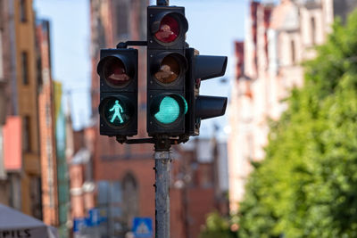 Traffic semaphore with green light and green figure of pedestrian on defocused city street, closeup