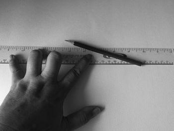 Cropped hand holding ruler and pencil on table