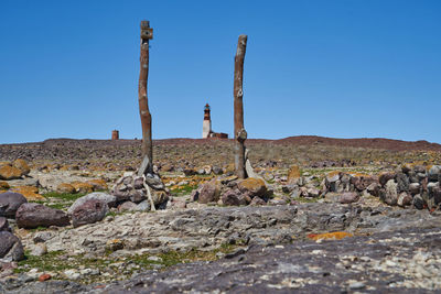 Lighthouse built of red bricks, located on a rocky island, framed in the middle of two wooden poles