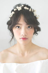 Close-up portrait of bride wearing flowers on hair against white background