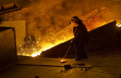 Full length of man working while standing by fire in factory