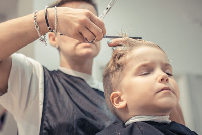 Close-up of female hairdresser styling boy hair in salon