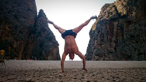 Shirtless man performing handstand at beach