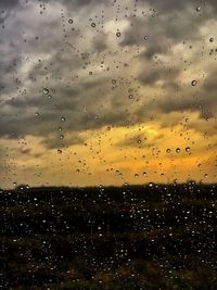 Close-up of wet glass against sky during sunset