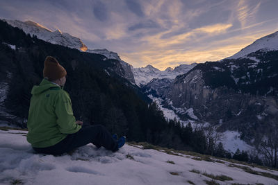 Mature man sitting on snowcapped mountain against sky during sunset