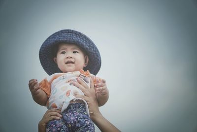 Cropped hands holding baby girl against sky