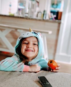 Portrait of smiling girl with apple sitting on table at home