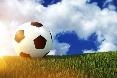 Close-up of soccer ball on field against cloudy sky