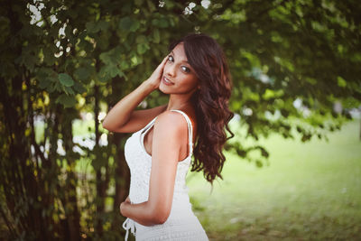 Side view of young woman standing by tree