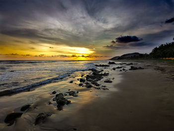 The sun contrasting with the sky, clouds, water, rocks and sand on the