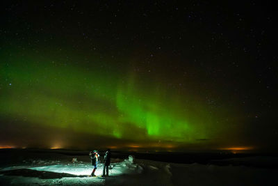 Hikers looking at northern lights while standing on snow covered field at night