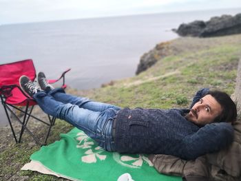 Portrait of man lying down on cliff by sea