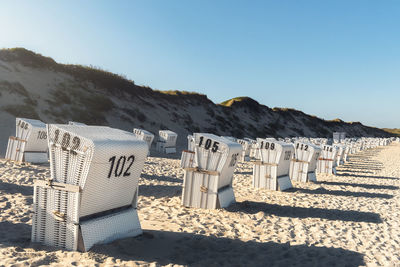 Hooded chairs on beach against clear blue sky