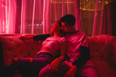 View of couple embracing while sitting on sofa in illuminated room