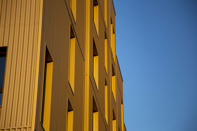 Low angle view of yellow building against clear blue sky