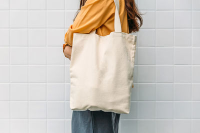 Midsection of woman holding bag while standing against wall
