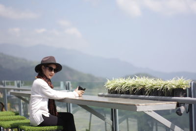 Side view of woman sitting on table on building terrace against sky