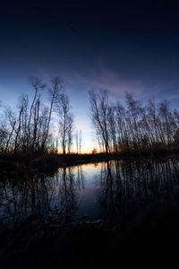 Silhouette bare trees by lake against sky during sunset