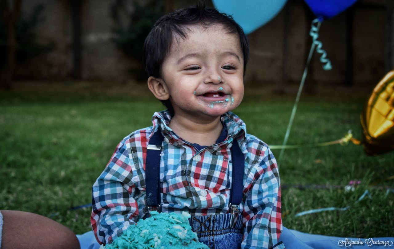 CLOSE-UP PORTRAIT OF HAPPY BOY WITH LAWN