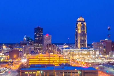 Illuminated buildings in city against clear blue sky