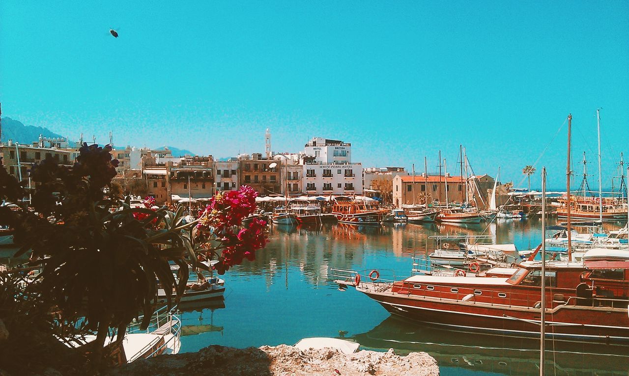 clear sky, built structure, building exterior, water, architecture, blue, nautical vessel, moored, copy space, boat, transportation, harbor, reflection, mode of transport, house, outdoors, day, river, residential structure, city