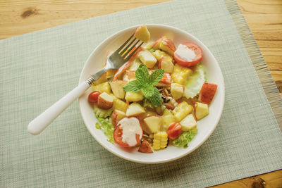 Mixed vegetable and fruit salad with crab sticks on a white plate, ready to serve