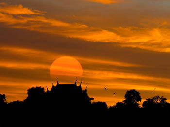 Silhouette trees against dramatic sky during sunset