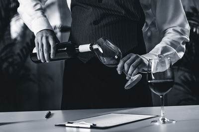 Midsection of bartendar pouring wine in glass