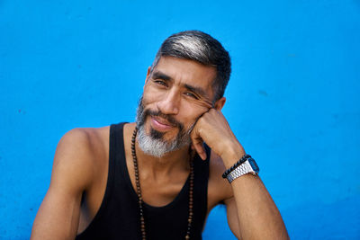 Close-up portrait of mature man sitting by blue wall