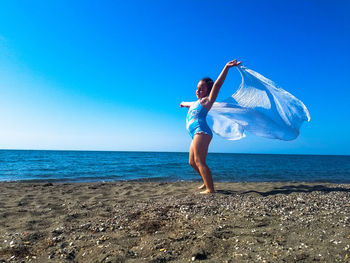 Girl standing on shore at beach against clear blue sky during sunny day