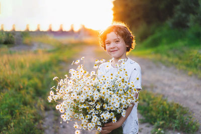 Cute smiling boy at camomile field at sunset in soft sunlight. boy and daisies.