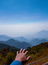 Cropped hand of person gesturing towards landscape against sky