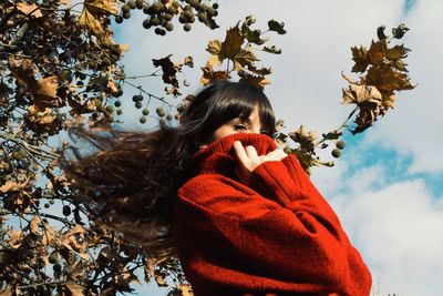 Low angle portrait of woman wearing warm clothing while standing against branches