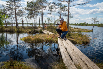 A woman with a camera sat down on a wooden walkway leading from the shore to an island on the lake